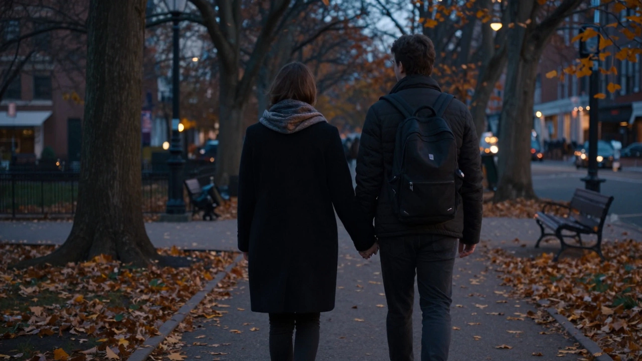Two people walking hand in hand through a park at dusk, autumn leaves falling around them.